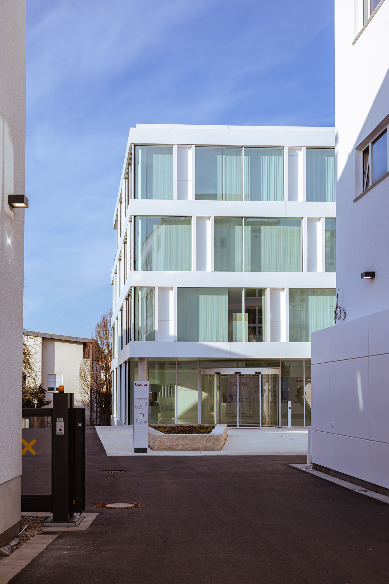 Modern white office building with large glass windows and a revolving glass entrance door.