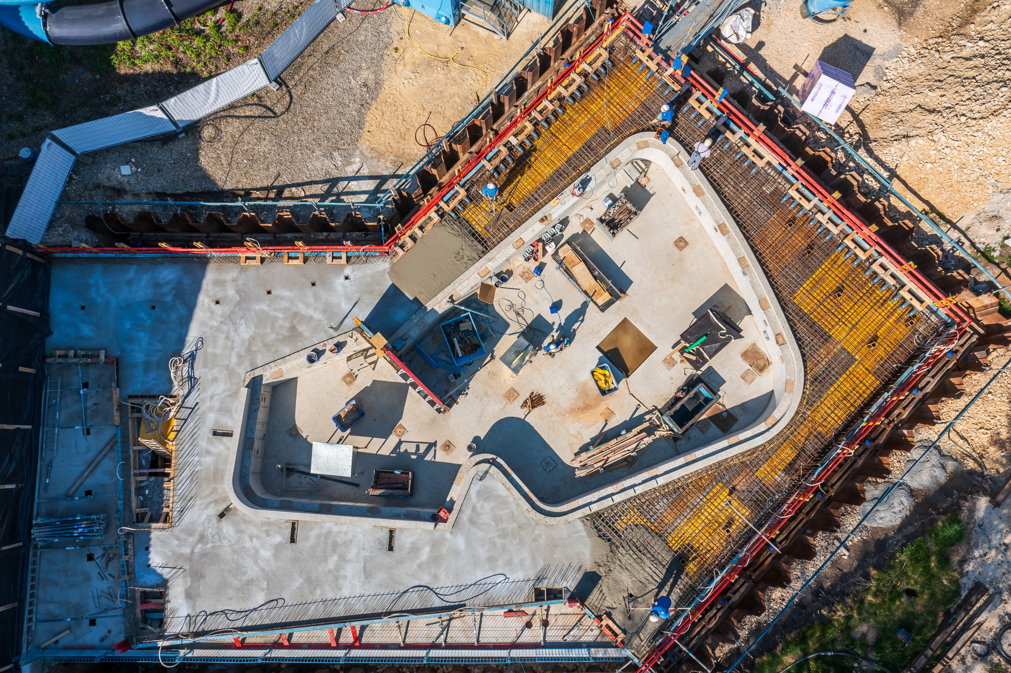 Aerial view of a construction site with workers, concrete foundation, rebar, and construction tools.