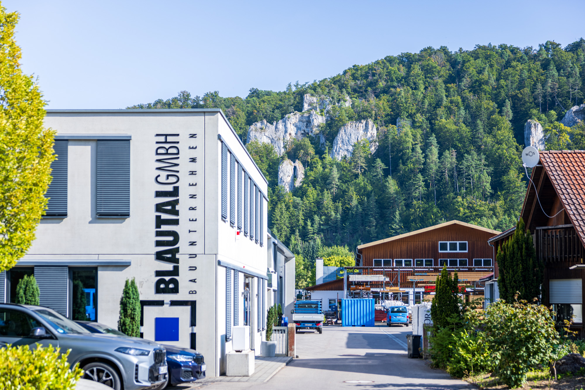 Industrial building with BLAUTAL GMBH signage next to parked cars and forested limestone cliffs in the background.