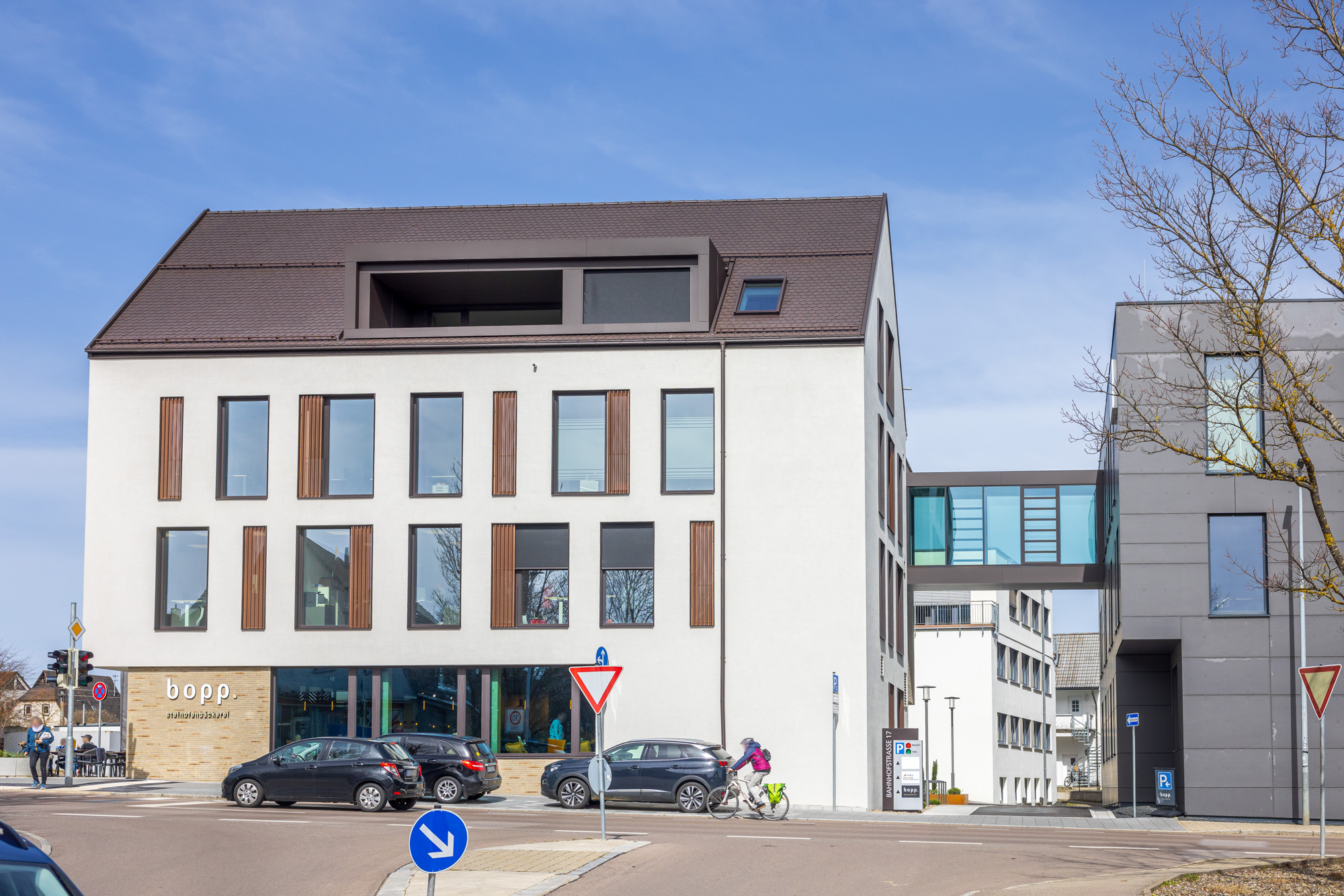 Modern three-story building with 'bopp.' restaurant on ground floor, cars parked in front and a cyclist riding by on a sunny day.